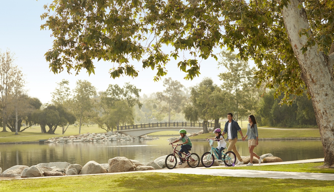 Exterior view of family riding bikes and walking at park in Irvine, CA.