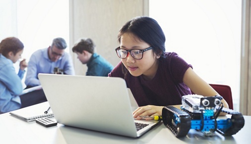 Focused girl student programming robotics at laptop in classroom