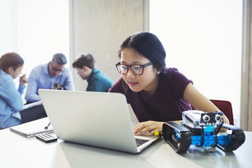Focused girl student programming robotics at laptop in classroom
