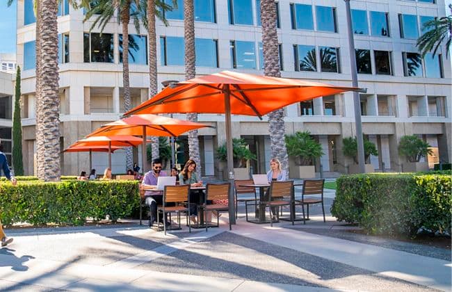 Exterior view of people at The Commons outdoor workspace at the 100 Spectrum Center Drive office building in Irvine, CA.