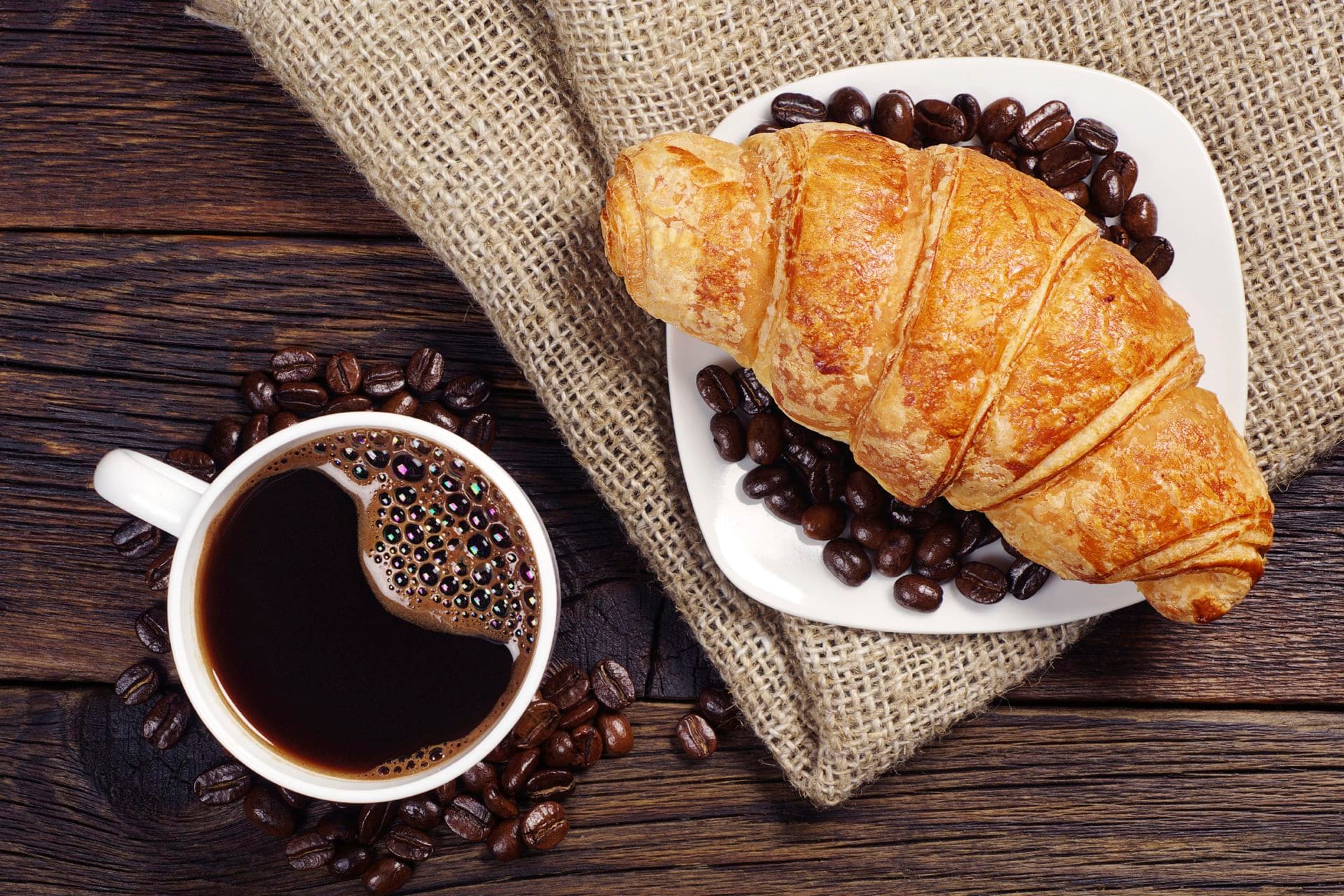 Cup of hot coffee with croissant for breakfast on a rustic wooden table, top view